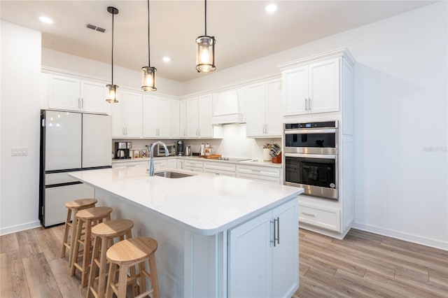 kitchen with sink, white refrigerator, double oven, custom range hood, and white cabinets