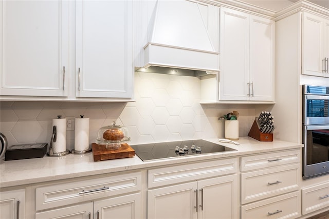 kitchen featuring premium range hood, white cabinets, backsplash, stainless steel double oven, and black electric cooktop