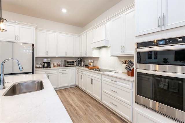 kitchen featuring sink, black electric stovetop, custom range hood, decorative light fixtures, and stainless steel double oven