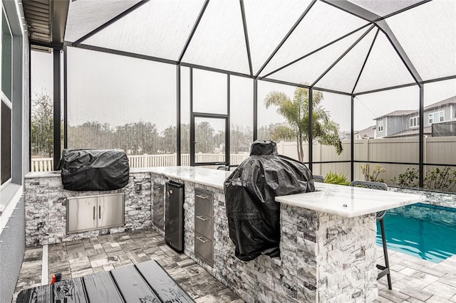 view of swimming pool featuring exterior bar, exterior kitchen, grilling area, glass enclosure, and a patio area