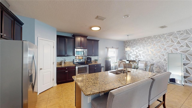 kitchen with pendant lighting, sink, light tile patterned floors, appliances with stainless steel finishes, and a kitchen island with sink