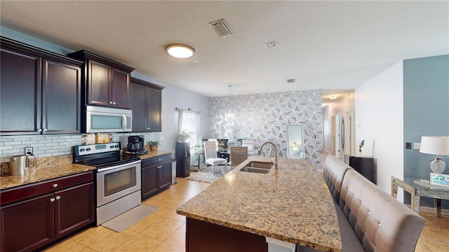 kitchen featuring light tile patterned floors, sink, a kitchen island with sink, hanging light fixtures, and stainless steel appliances