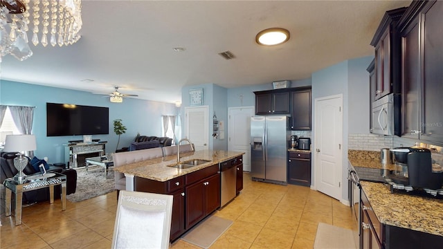 kitchen with appliances with stainless steel finishes, an island with sink, sink, backsplash, and ceiling fan