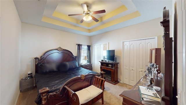 carpeted bedroom with a raised ceiling, two closets, and ceiling fan