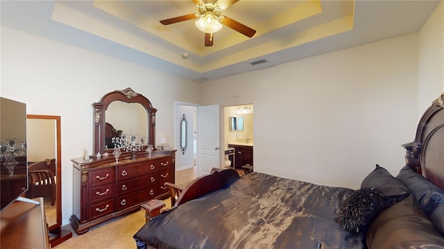 bedroom with ceiling fan, ensuite bath, a raised ceiling, and light carpet