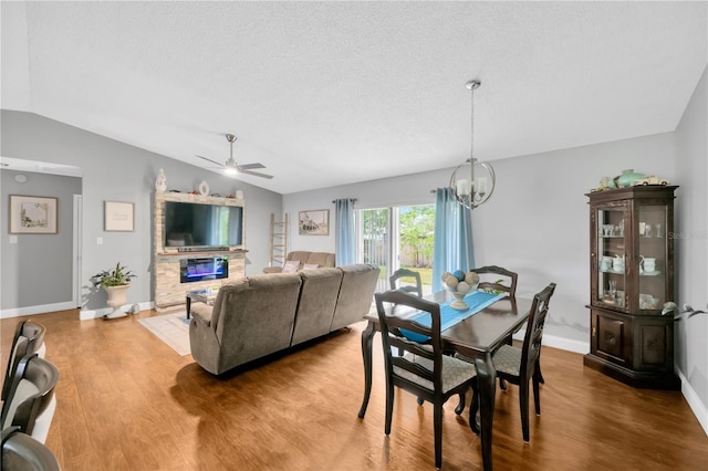 dining room featuring hardwood / wood-style flooring, vaulted ceiling, ceiling fan with notable chandelier, and a textured ceiling