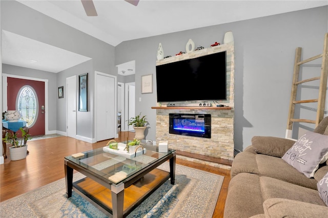 living room with ceiling fan, lofted ceiling, a stone fireplace, and hardwood / wood-style floors