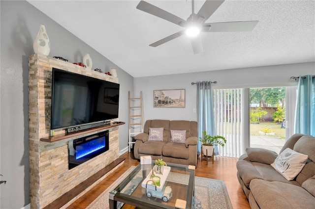 living room with hardwood / wood-style flooring, ceiling fan, a textured ceiling, a stone fireplace, and vaulted ceiling