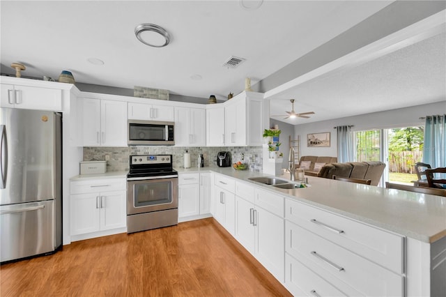 kitchen featuring stainless steel appliances, kitchen peninsula, sink, and white cabinets