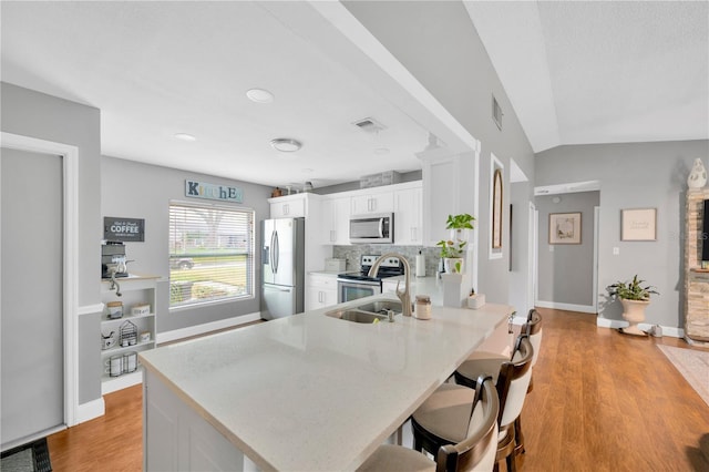 kitchen with vaulted ceiling, a breakfast bar, white cabinetry, kitchen peninsula, and stainless steel appliances