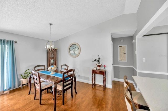 dining room featuring hardwood / wood-style floors, a textured ceiling, vaulted ceiling, and a chandelier