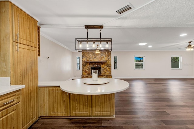 kitchen with pendant lighting, crown molding, dark hardwood / wood-style flooring, a stone fireplace, and kitchen peninsula