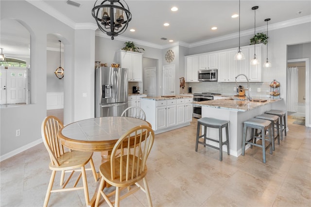 kitchen with stainless steel appliances, light stone countertops, a center island with sink, and white cabinets