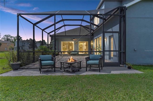 patio terrace at dusk featuring a fire pit, a lanai, a lawn, and ceiling fan