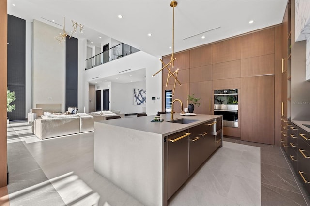 kitchen with sink, a high ceiling, hanging light fixtures, a kitchen island with sink, and stainless steel appliances