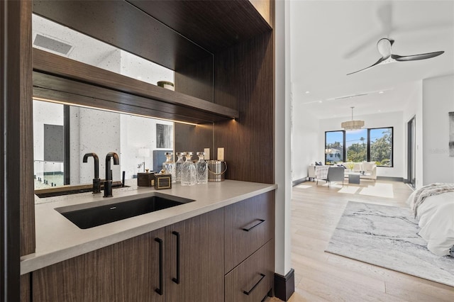 bar with ceiling fan, light hardwood / wood-style floors, sink, and dark brown cabinets
