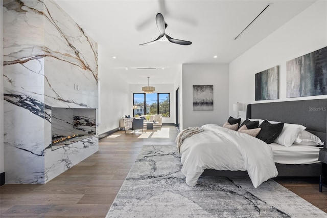 bedroom featuring a tiled fireplace, wood-type flooring, and ceiling fan