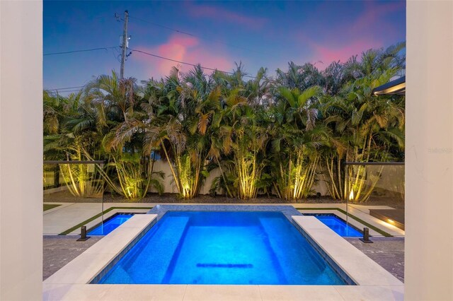 pool at dusk featuring an in ground hot tub