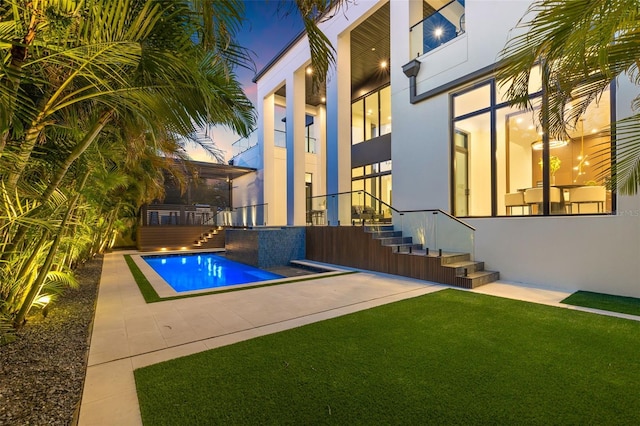 pool at dusk featuring a patio area and a lawn