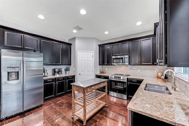 kitchen with sink, dark wood-type flooring, backsplash, stainless steel appliances, and light stone countertops