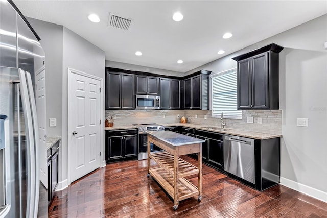 kitchen with stainless steel appliances, light stone countertops, sink, and dark wood-type flooring