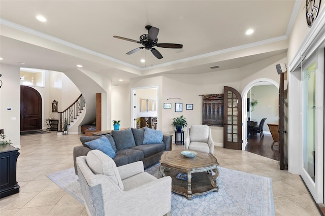 tiled living room with a tray ceiling, ornamental molding, french doors, and ceiling fan