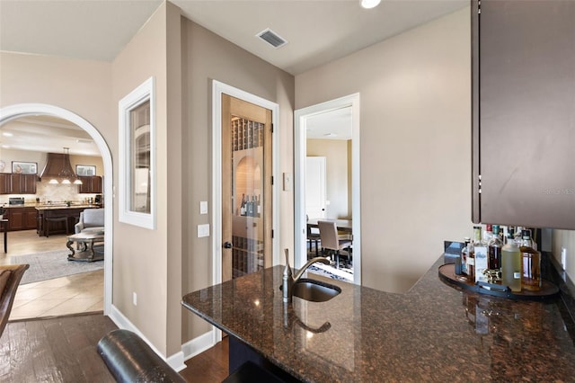 kitchen with sink, custom exhaust hood, tasteful backsplash, dark stone countertops, and hardwood / wood-style flooring