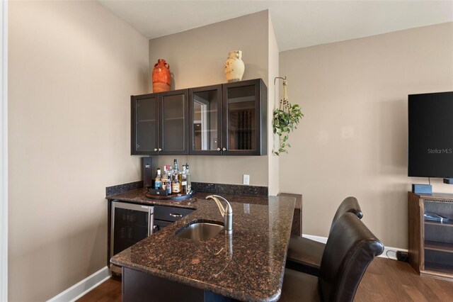 kitchen featuring sink, dark wood-type flooring, dark stone countertops, dark brown cabinets, and wine cooler