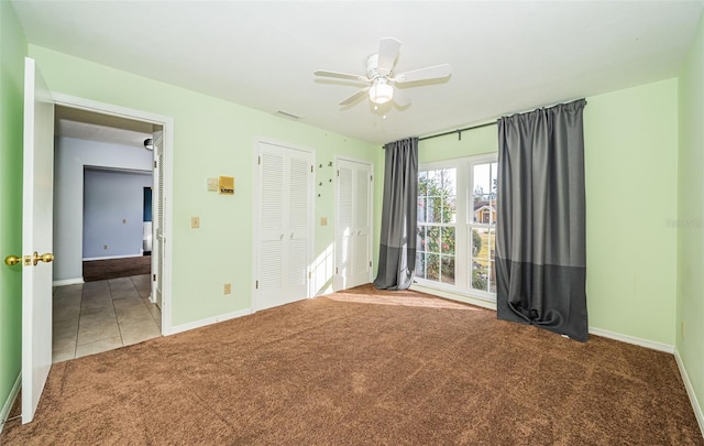 unfurnished bedroom featuring ceiling fan, carpet floors, and multiple closets