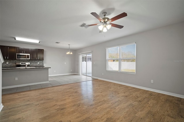 unfurnished living room featuring sink, ceiling fan with notable chandelier, and light wood-type flooring