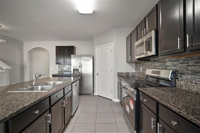 kitchen featuring sink, light tile patterned floors, appliances with stainless steel finishes, backsplash, and dark brown cabinetry