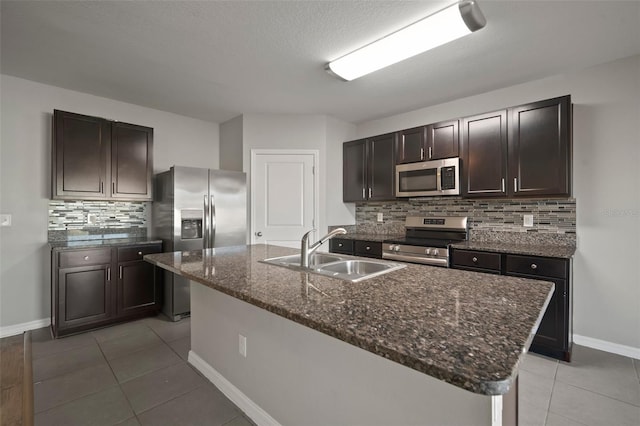 kitchen featuring light tile patterned flooring, appliances with stainless steel finishes, sink, a kitchen island with sink, and dark brown cabinetry