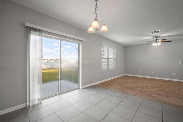 tiled empty room featuring ceiling fan with notable chandelier