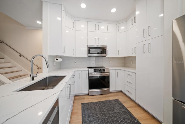 kitchen with white cabinetry, appliances with stainless steel finishes, decorative backsplash, and light hardwood / wood-style flooring