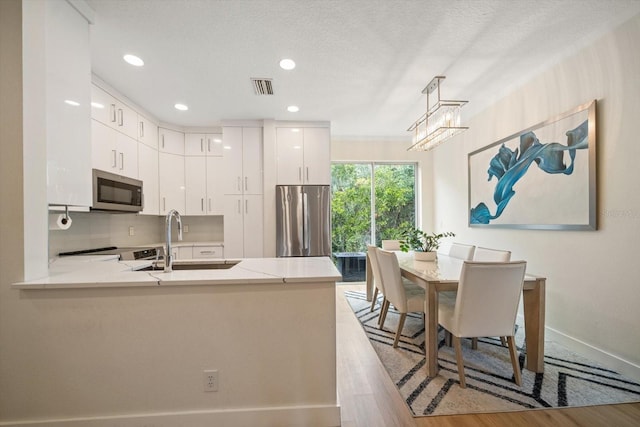 kitchen featuring appliances with stainless steel finishes, pendant lighting, sink, white cabinets, and kitchen peninsula