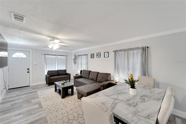 living room featuring ceiling fan, ornamental molding, light hardwood / wood-style floors, and a textured ceiling