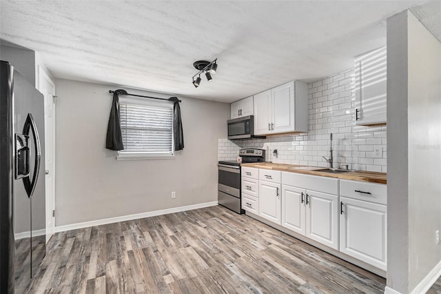 kitchen featuring wooden counters, stainless steel appliances, white cabinets, decorative backsplash, and light wood-type flooring