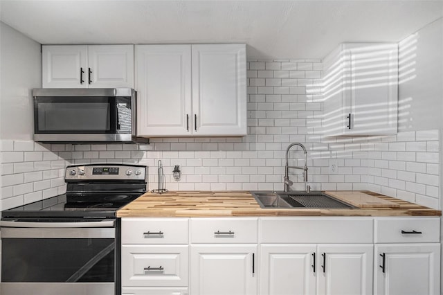 kitchen with white cabinetry, sink, stainless steel appliances, and butcher block countertops