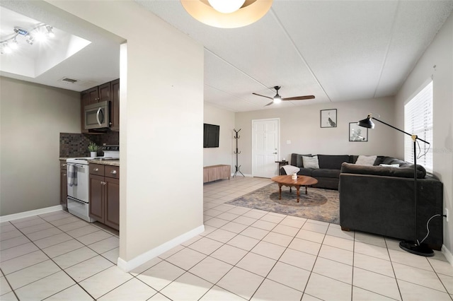 tiled living room with ceiling fan and a tray ceiling