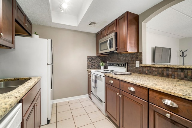 kitchen featuring light tile patterned floors, white appliances, light stone counters, decorative backsplash, and a raised ceiling