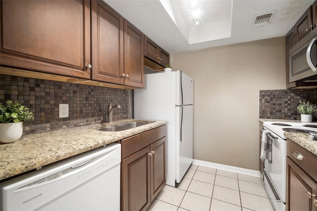 kitchen with sink, light stone counters, a textured ceiling, and white appliances