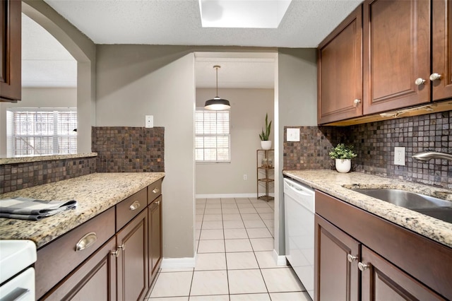 kitchen featuring sink, light tile patterned floors, white dishwasher, pendant lighting, and light stone countertops