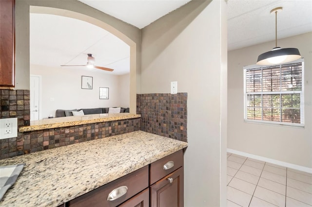 kitchen with ceiling fan, hanging light fixtures, tasteful backsplash, light stone countertops, and light tile patterned flooring