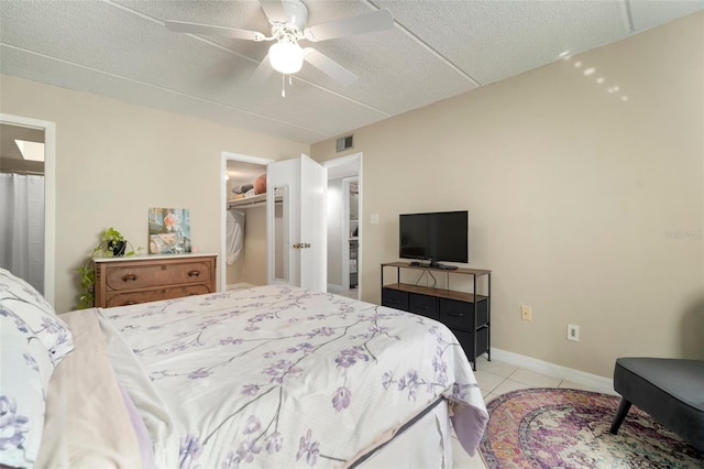 bedroom featuring light tile patterned flooring, a walk in closet, a textured ceiling, and ceiling fan