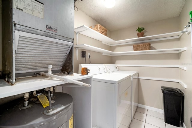 clothes washing area with light tile patterned floors, washing machine and dryer, water heater, and a textured ceiling