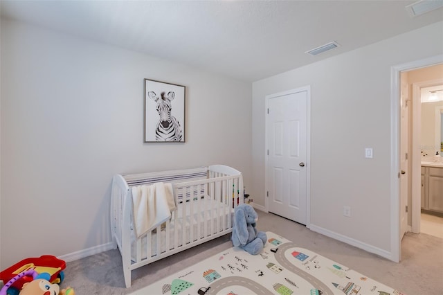 bedroom featuring light carpet, connected bathroom, and a crib