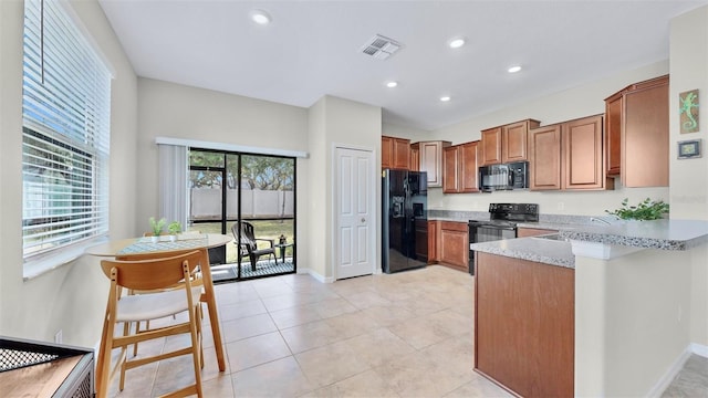 kitchen featuring a breakfast bar area, light stone countertops, black appliances, light tile patterned flooring, and kitchen peninsula