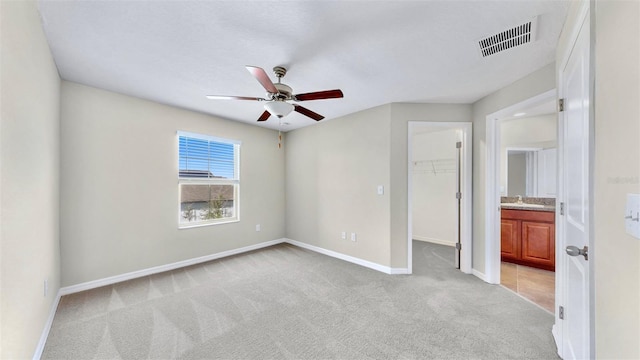 unfurnished bedroom with ensuite bathroom, a spacious closet, light colored carpet, a closet, and ceiling fan