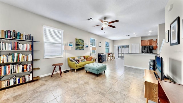living room with light tile patterned floors, visible vents, baseboards, and ceiling fan