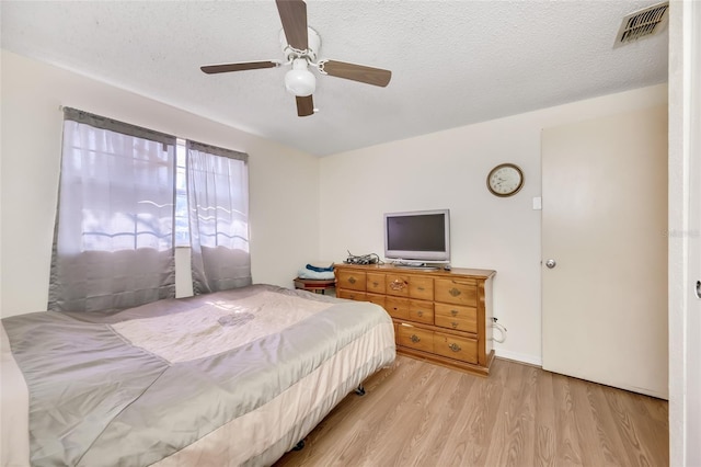 bedroom with ceiling fan, light hardwood / wood-style floors, and a textured ceiling